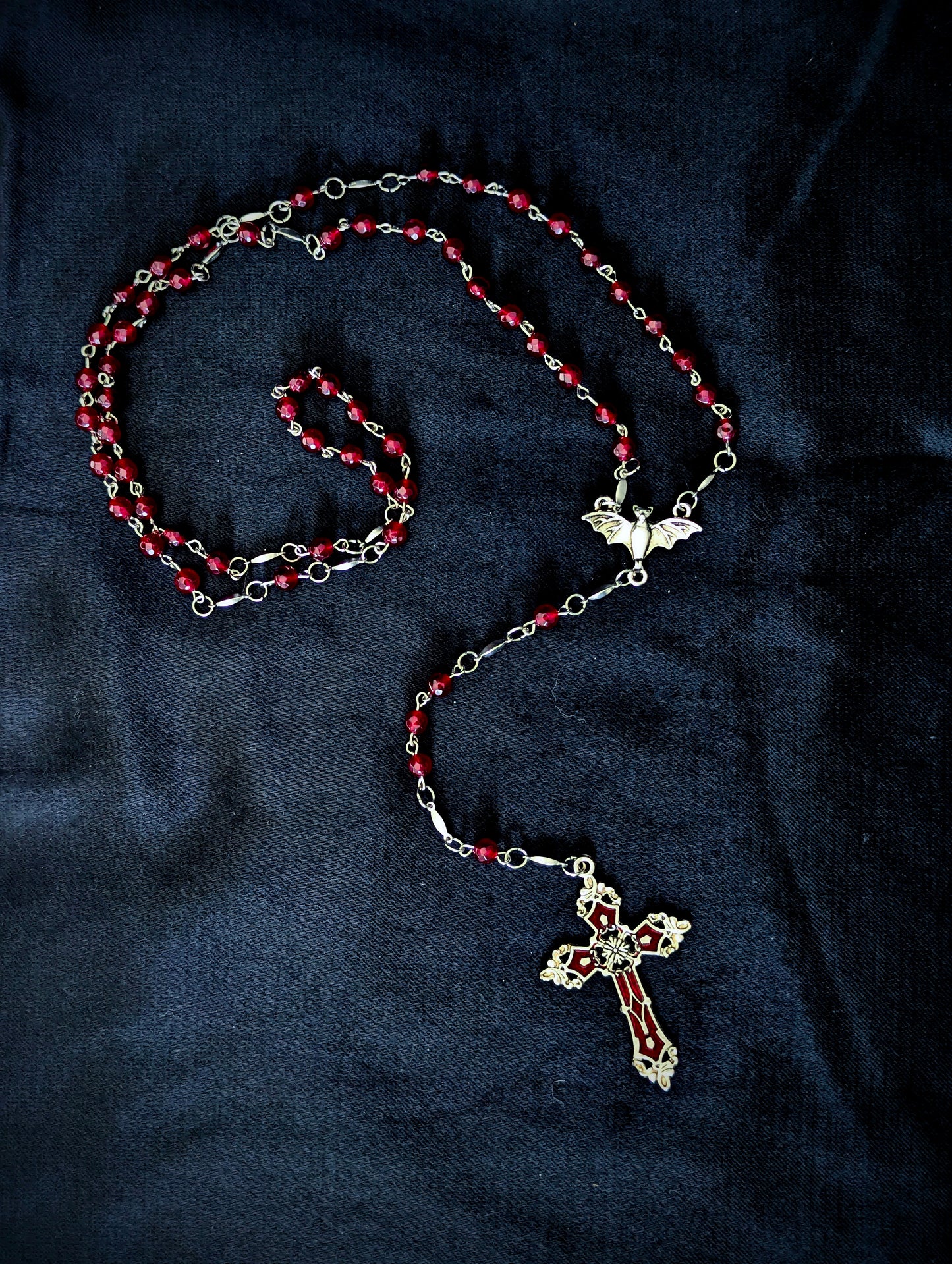 Rosary with red beads and silver cross on a dark fabric background