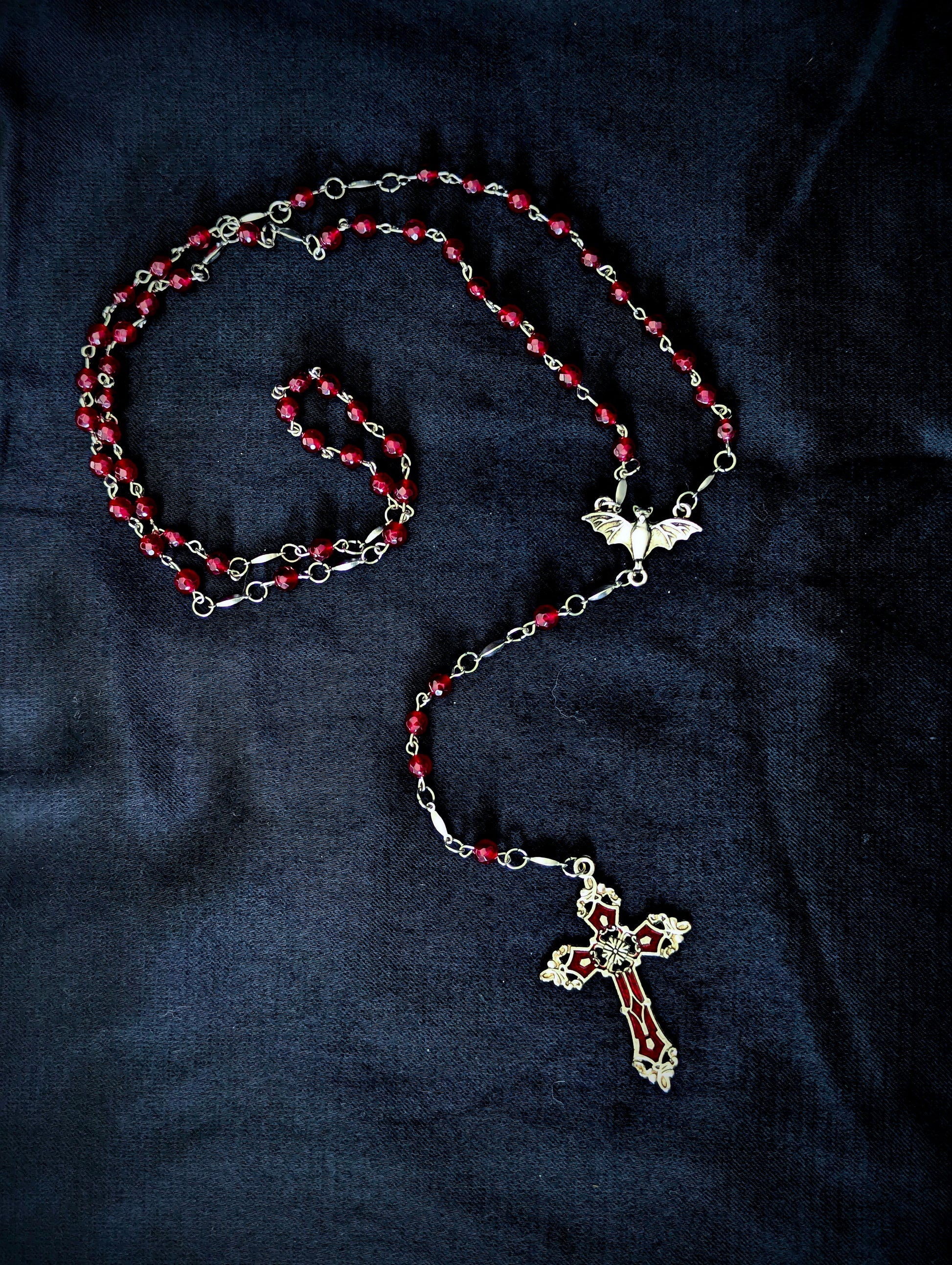 Rosary with red beads and silver cross on a dark fabric background