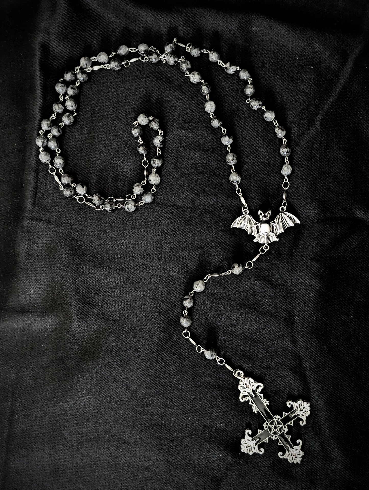Silver rosary with a cross and bat pendant on a dark fabric background