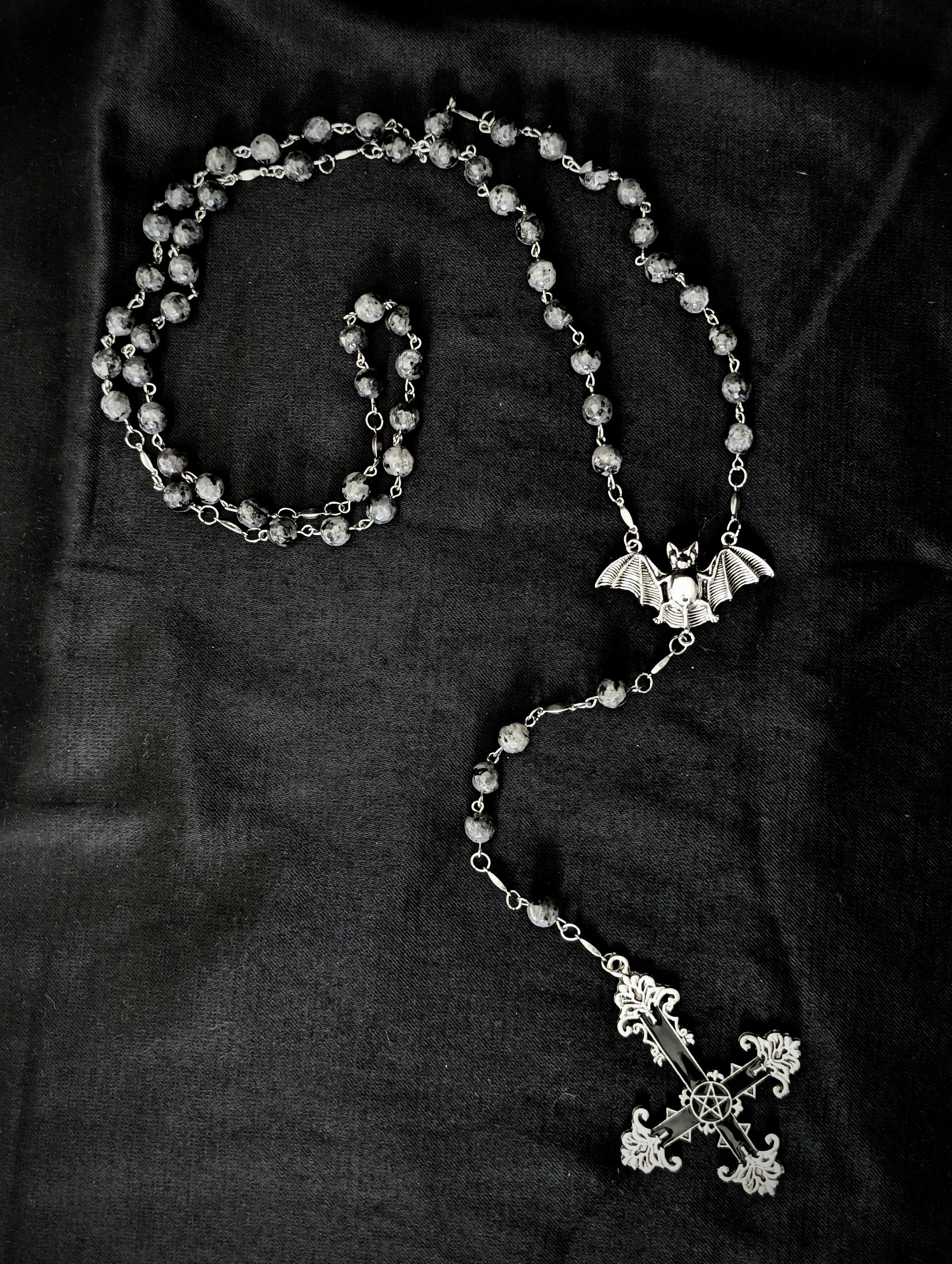 Silver rosary with a cross and bat pendant on a dark fabric background