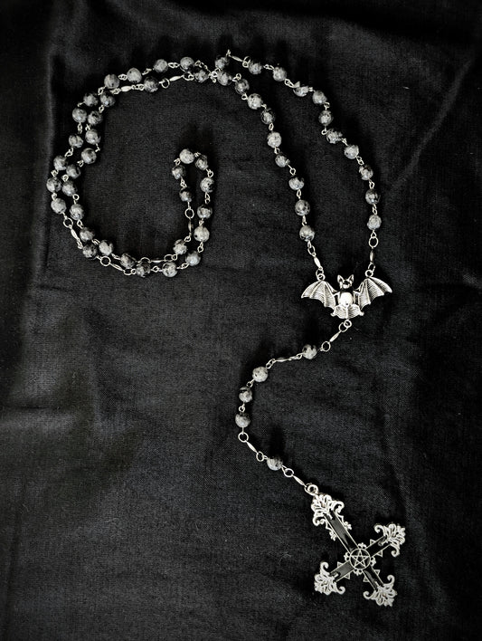 Silver rosary with a cross and bat pendant on a dark fabric background