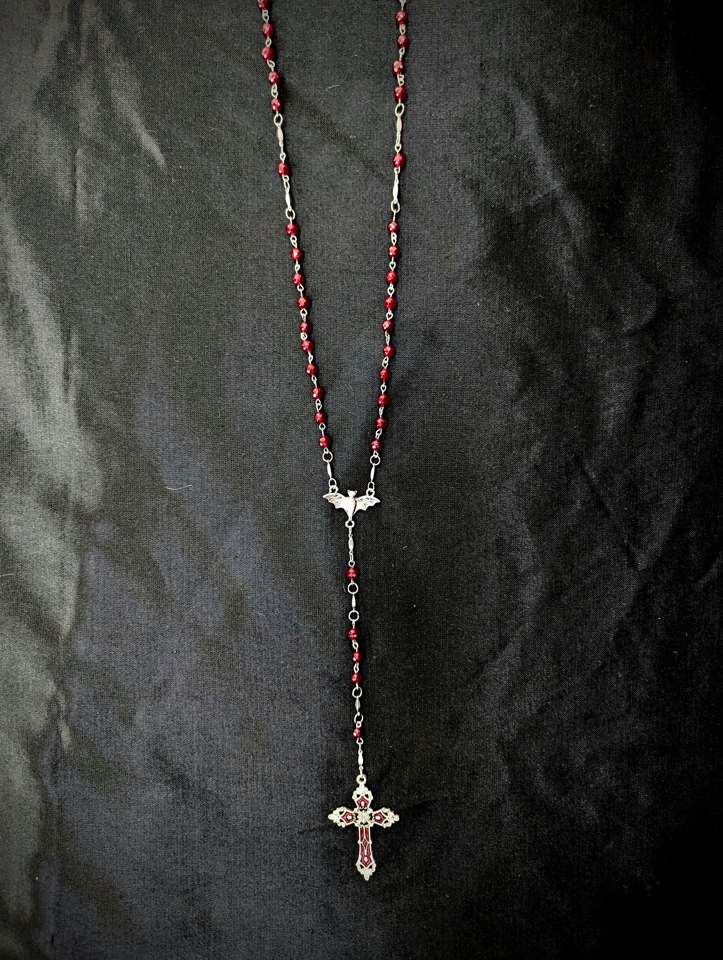 Rosary necklace with red beads and a cross pendant on a dark fabric background
