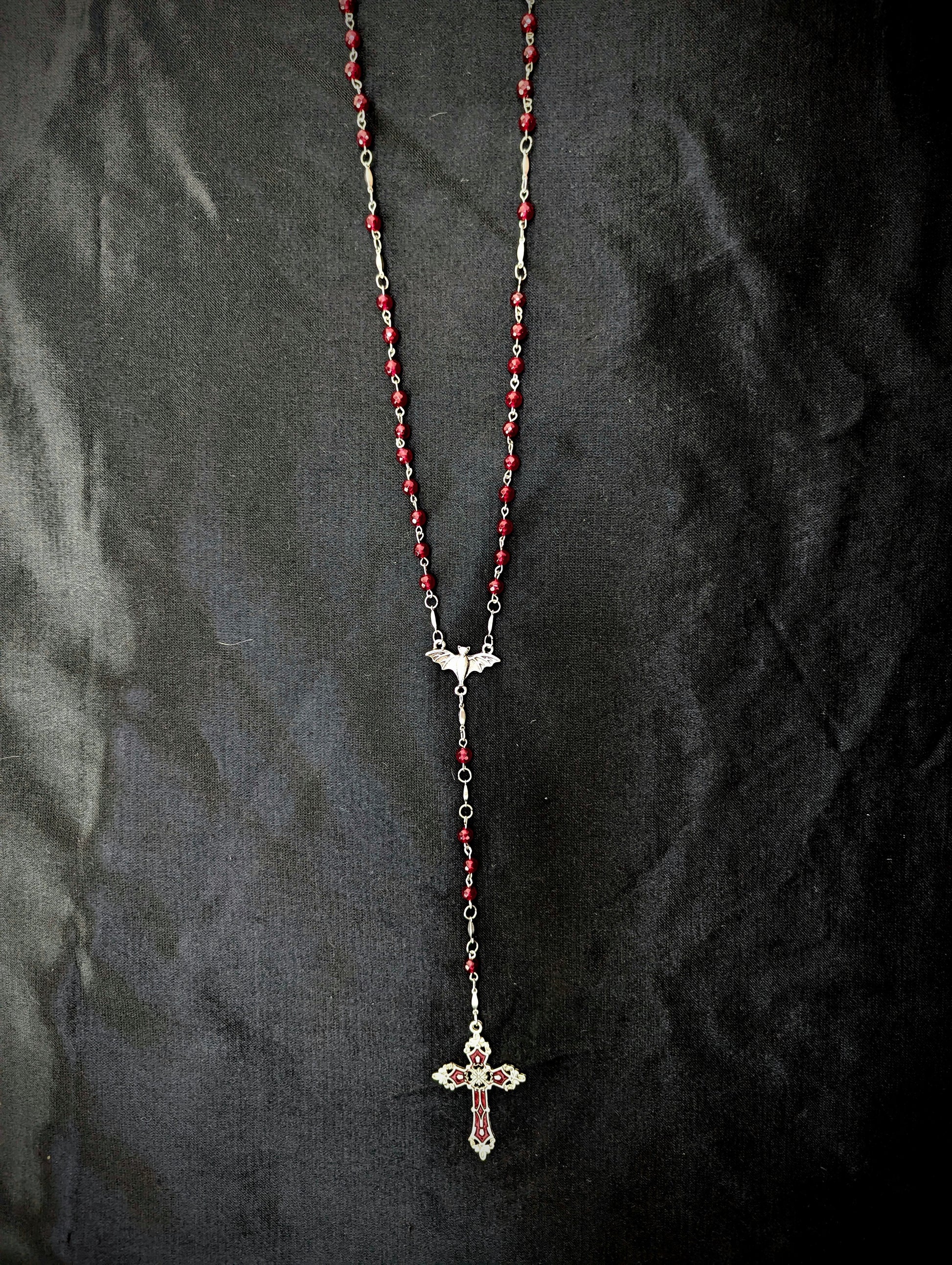 Rosary necklace with red beads and a cross pendant on a dark fabric background