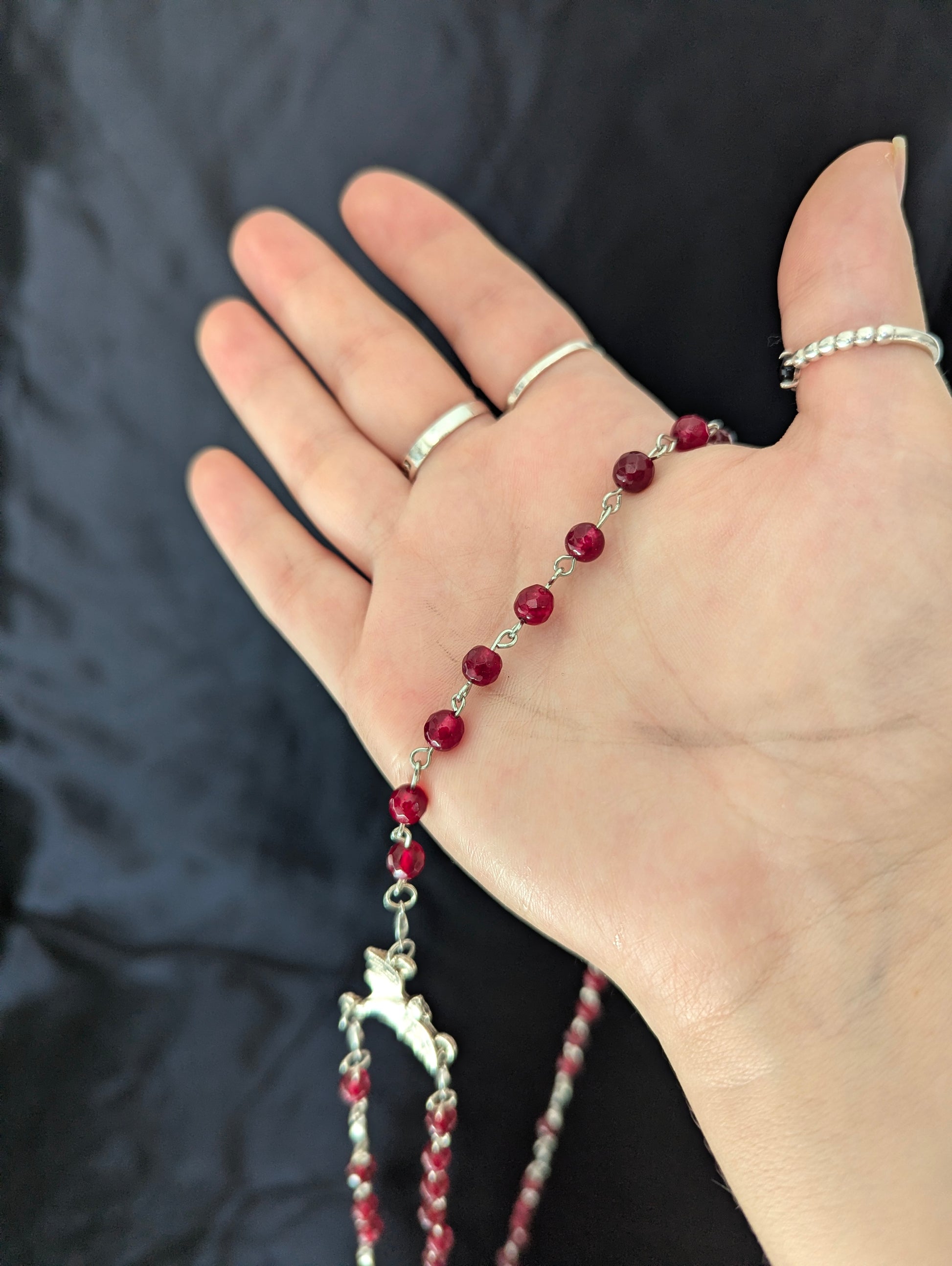 Hand wearing a silver bracelet with red beads on a dark background