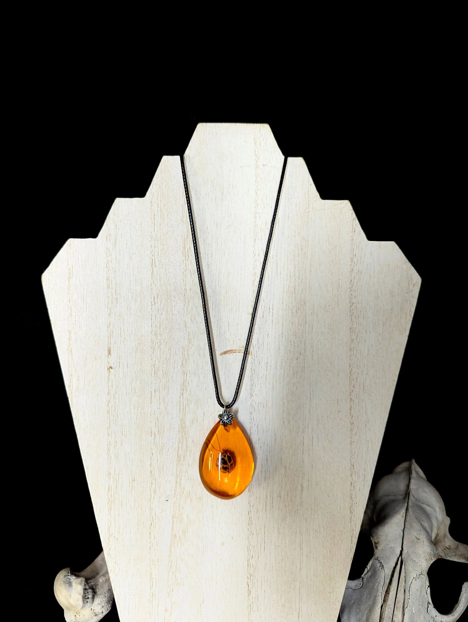 Amber teardrop pendant necklace on a white wooden stand with a black background