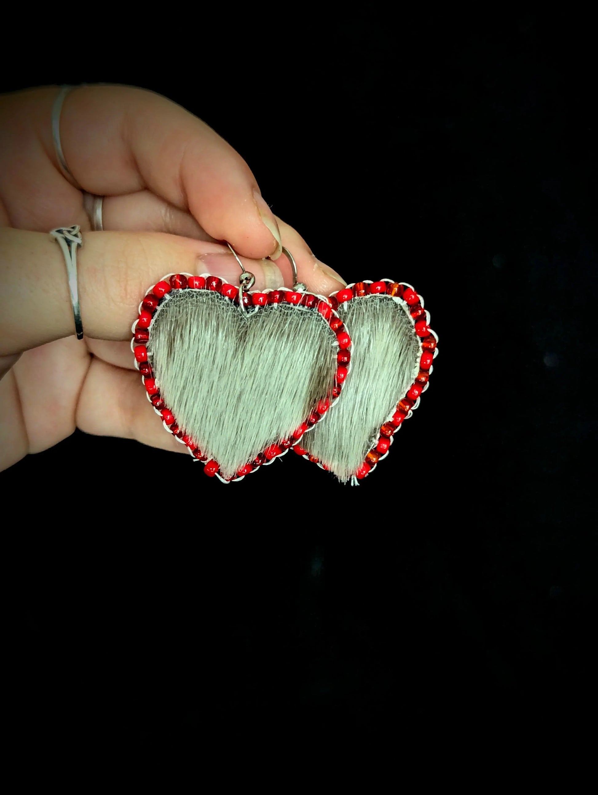 Heart-shaped earrings with red accents held by a hand against a black background