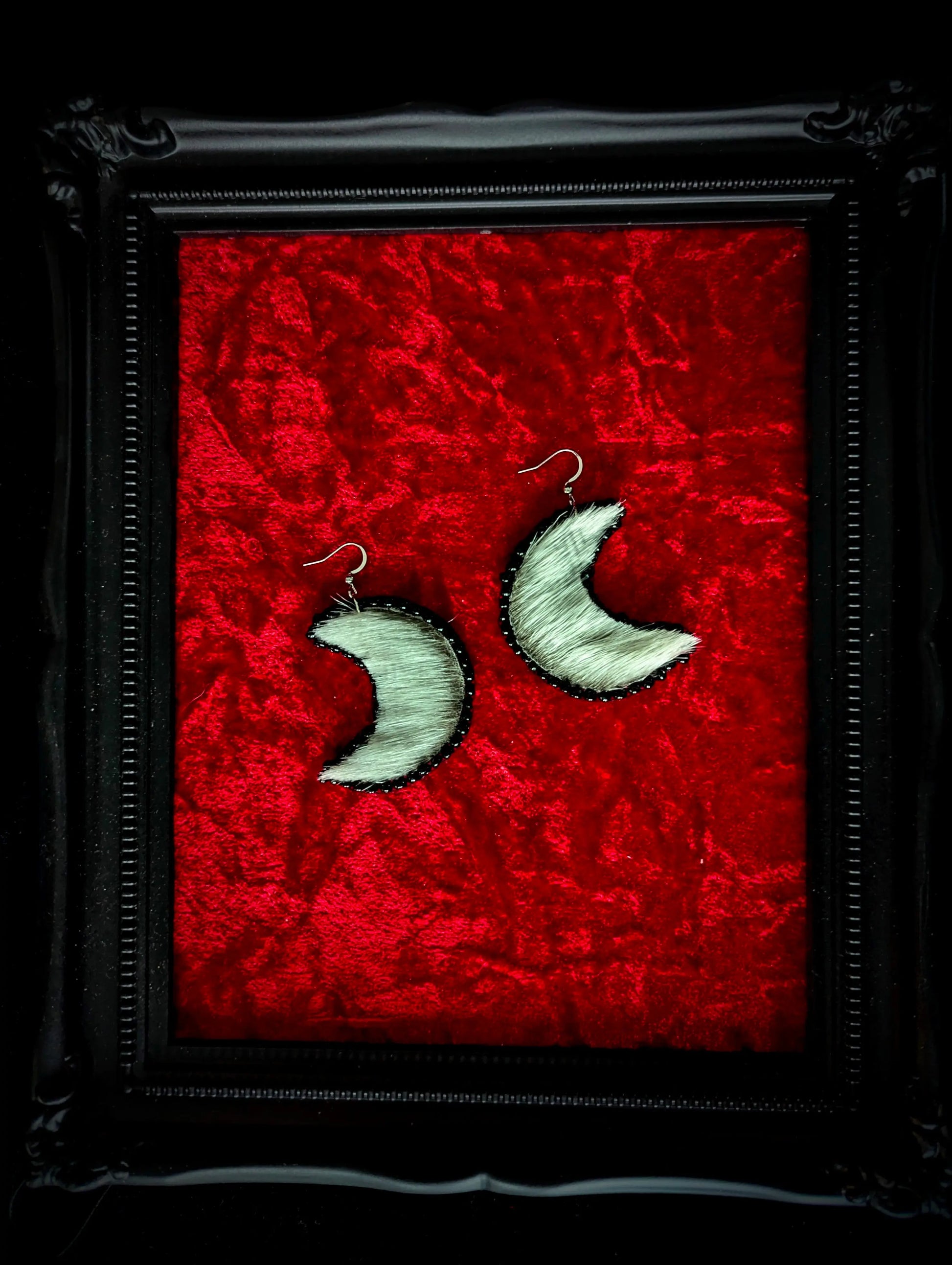 Moon-shaped earrings on a red textured background with a black frame.