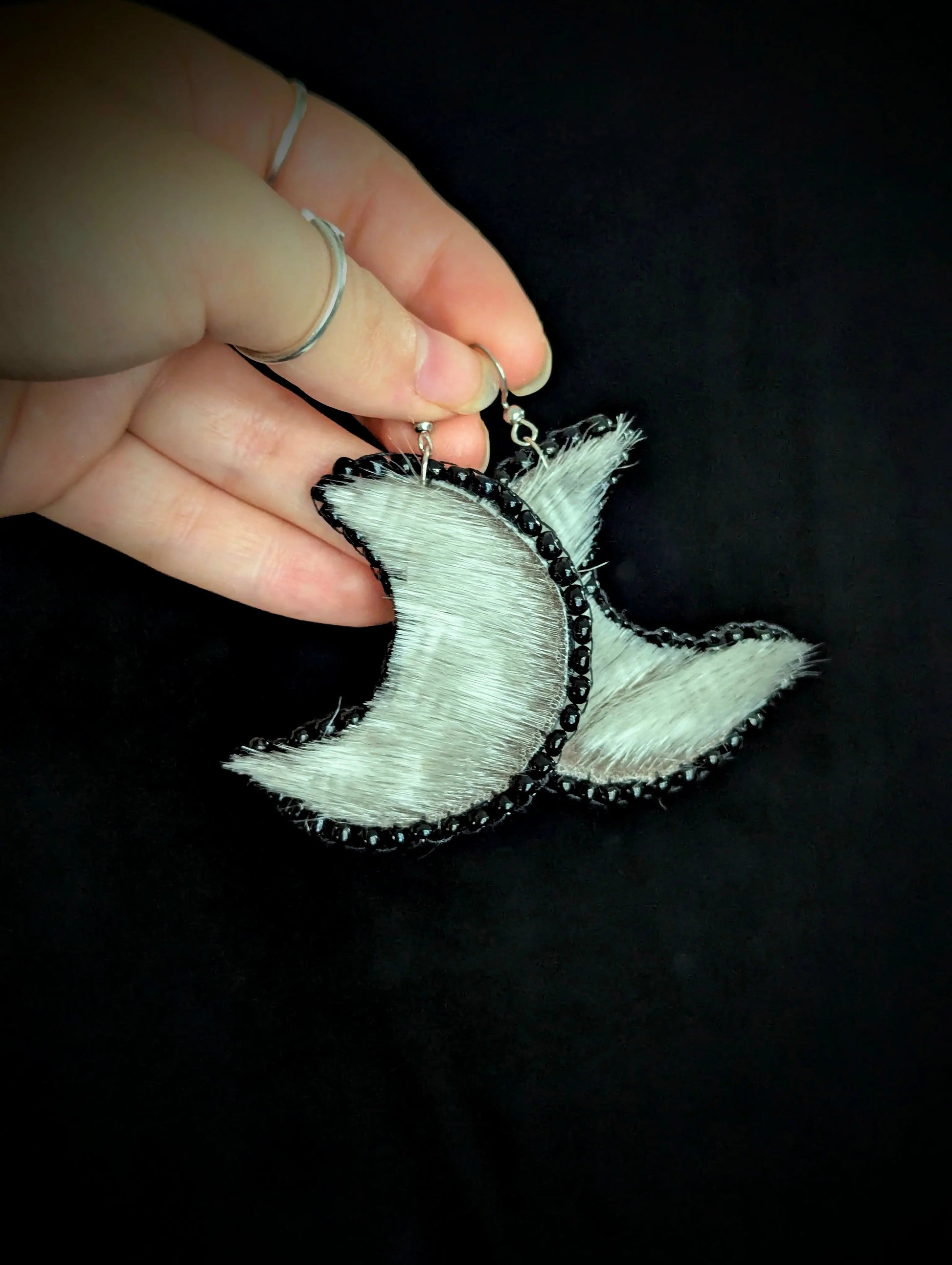 Hand holding a crescent moon-shaped earring against a black background